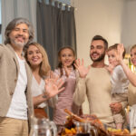 cheerful-mature-man-with-smartphone-making-selfie-with-grandchildren-his-wife-their-daughter-her-husband-waving-hands-by-festive-table