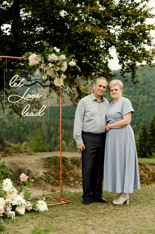 elderly-wedding-couple-stands-near-stylish-wedding-arch-tree-against-backdrop-mountains-old-groom-bride